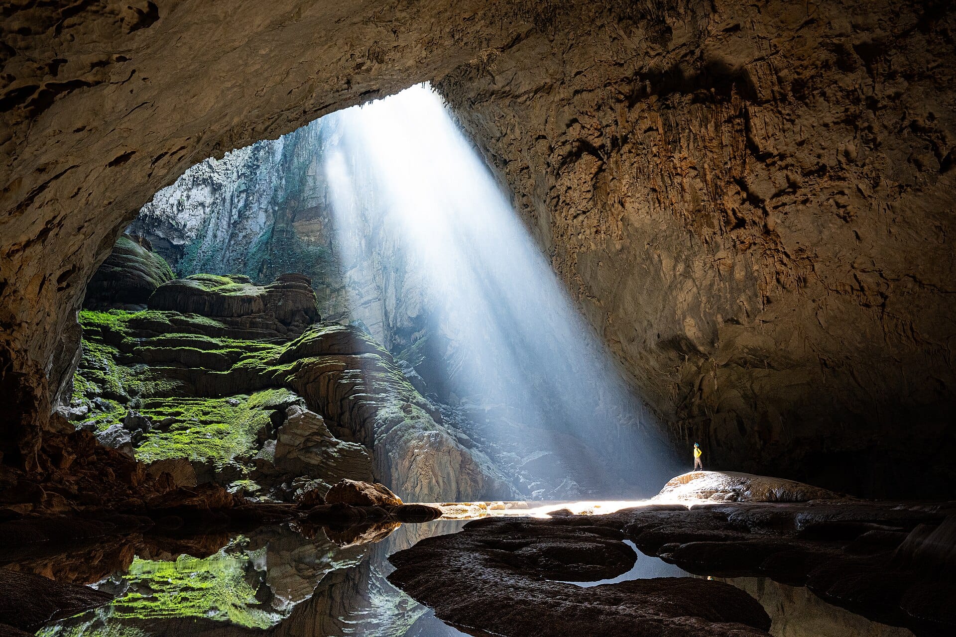 The first doline in Son Doong. A doline is an opening left where the cave roof collapsed, and sunlight pours through it. A lone person stands beside the beam. Photo: Trantuanviet (CC BY-SA 4.0, Wikimedia Commons)