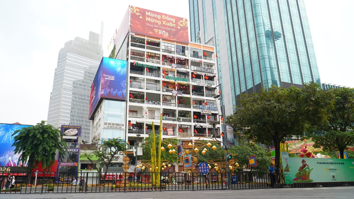 The Cafe Apartment after its February 2026 repaint, a white nine-storey block with a different shop sign on every balcony