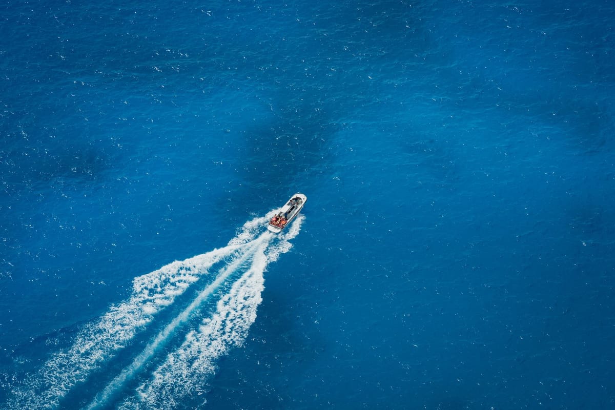 Aerial view of a lone tourist speedboat crossing a deep blue open sea, leaving a long white wake