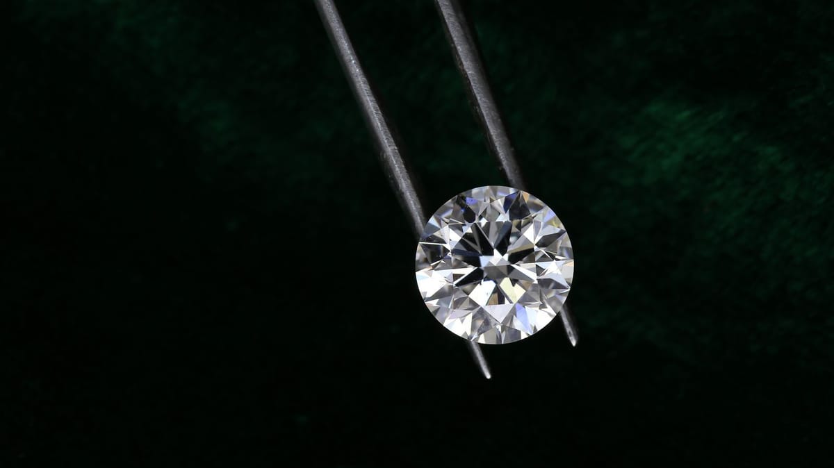 A round brilliant-cut diamond held in grading tweezers against a dark green velvet background