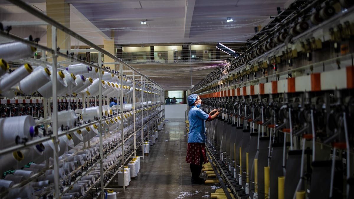 A lone worker tends towering rows of spinning machines inside a textile mill