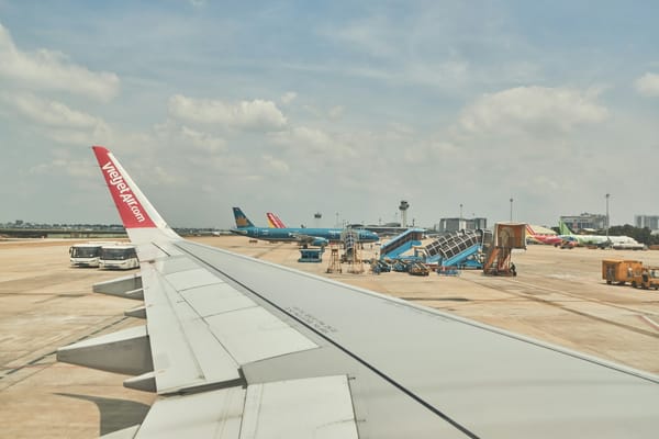 View from a VietJet aircraft wing over the tarmac at Tan Son Nhat airport in Ho Chi Minh City, with Vietnam Airlines and other jets parked in the distance