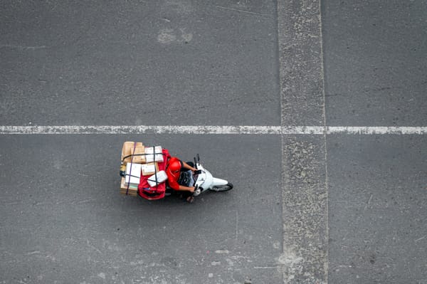 Aerial view of a delivery rider on a motorbike loaded with parcels crossing an empty road