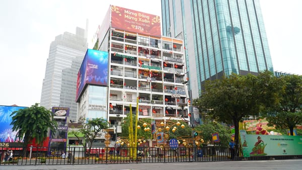 The Cafe Apartment after its February 2026 repaint, a white nine-storey block with a different shop sign on every balcony
