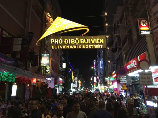 Bui Vien Walking Street at night, with the golden "Phố đi bộ Bùi Viện" sign spanning the street above crowds and neon lights