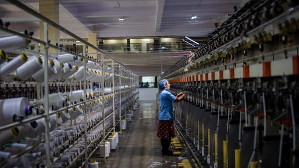 A lone worker tends towering rows of spinning machines inside a textile mill